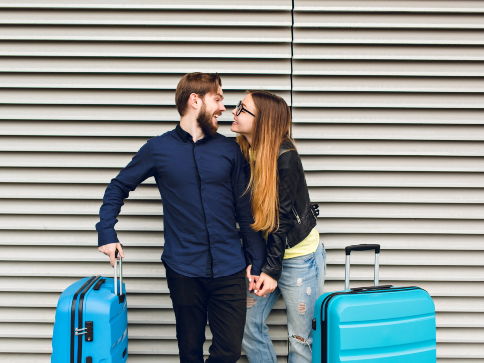 Portrait of cute couple  standing on gray  striped background.  She has long hair, glasses,  yellow sweater, jacket. He wears black shirt, beard. They are  hugging and smilinhg to each other.